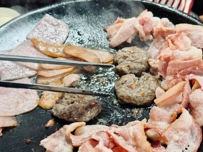 솥뚜껑 위에서 익어가는 햄, 베이컨, 소시지