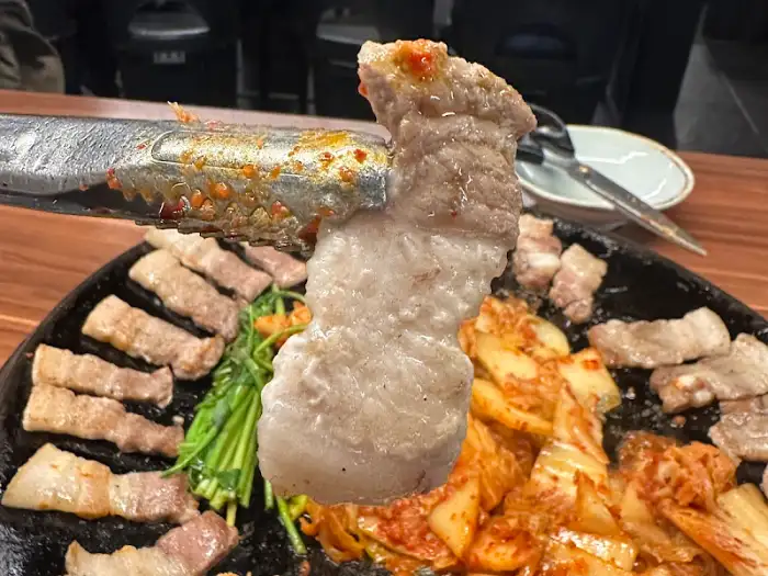 집게로 집어 올린 삼겹살 덩어리