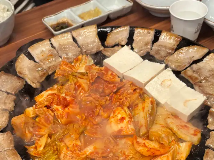 삼겹살, 김치, 두부가 함께 익어가고 있는 무쇠판