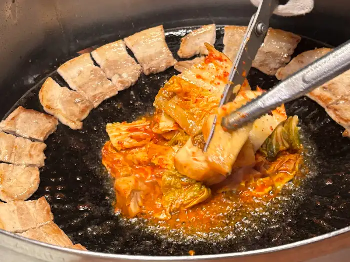 집게와 가위로 삼겹살과 김치를 집는 모습