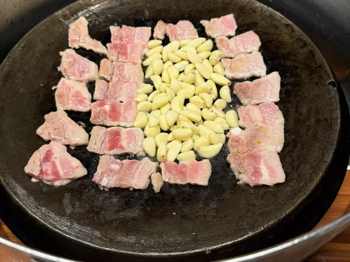 무쇠판 위에 놓인 삼겹살 조각들과 마늘