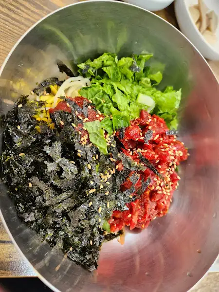 육회비빔밥은 알록달록한 재료들이 푸짐하게 담겨 있습니다. 밥, 채소, 육회, 김까지 조화롭게 어우러져 먹음직스럽습니다.