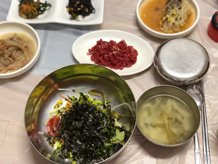 테이블에 다양한 밑반찬과 함께 육회비빔밥 그릇, 그리고 국물이 담긴 그릇이 놓여 있습니다.