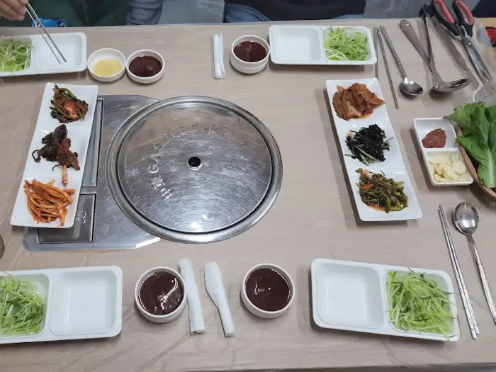 테이블 위에 숯불 그릴과 함께 여러 가지 밑반찬들이 가지런히 놓여 있습니다. 식사를 준비하는 듯한 모습입니다.