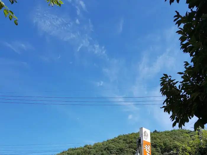 푸른 하늘과 산을 배경으로 서 있는 [상호명]의 간판.