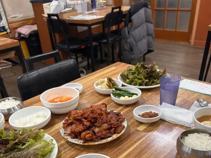 붉은 양념의 석쇠 불고기가 중앙에 놓여 있고, 쌈 채소와 밥이 준비된 모습
