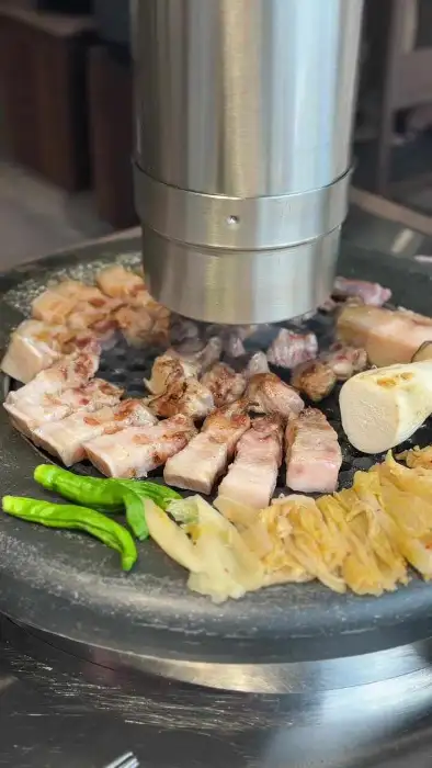 숯불 위에서 익어가는 흑돼지와 곁들임 채소들의 모습.
