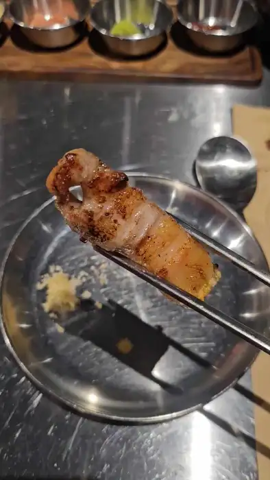 집게로 구워진 흑돼지 조각을 접시에 옮기는 모습.