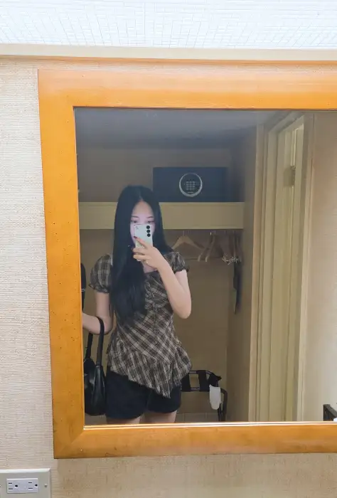 거울 셀카를 찍고 있는 여성의 모습. 빈티지한 프레임의 거울과 뒤편의 수납장, 옷걸이 등이 어우러져 공간의 분위기를 보여줍니다.
