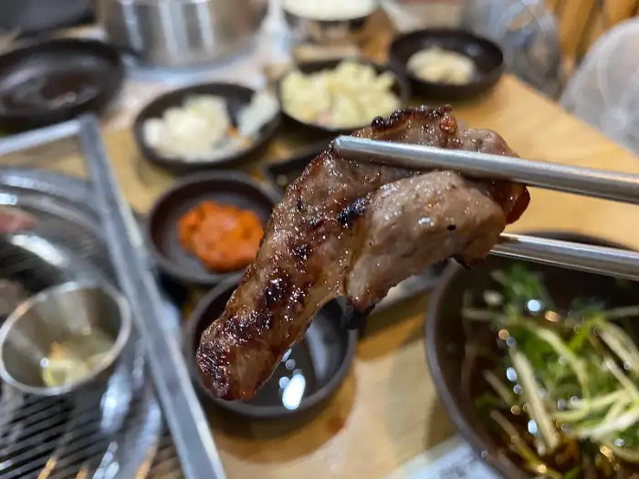 집게에 집힌 잘 익은 소고기 한 점. 겉면은 노릇하고 속은 촉촉해 보입니다.