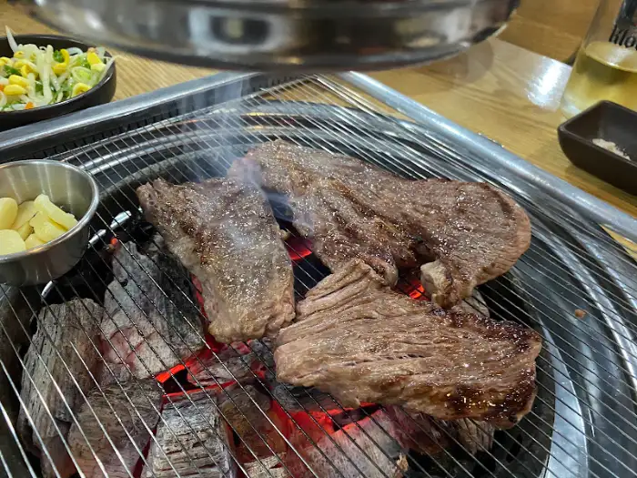 숯불 위에서 구워지고 있는 소고기 스테이크 같은 두툼한 고기 조각들.