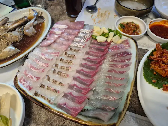 신선한 자연산 회가 푸짐하게 담겨 있는 커다란 접시. 두툼하게 썰린 회는 다양한 빛깔과 식감을 자랑하며, 곁들임으로 마늘과 고추가 준비되어 있다.