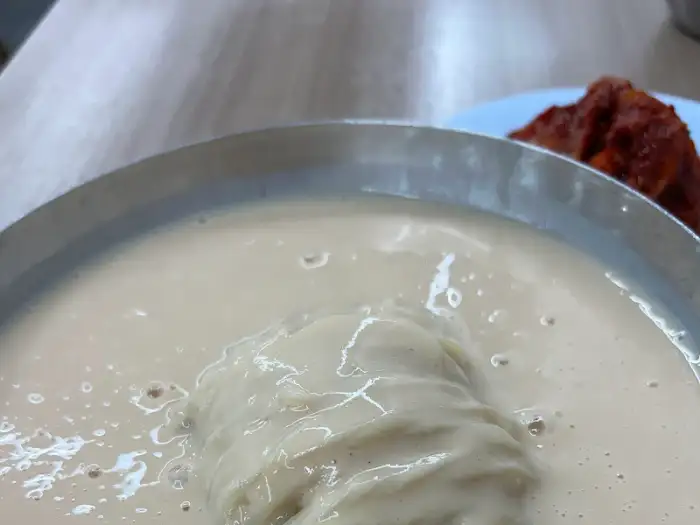 면발이 담긴 콩국수 그릇에 국자를 넣은 모습