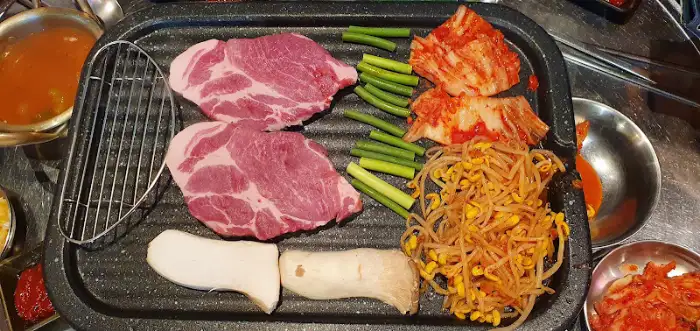 불판 위에 얹어진 생고기, 김치, 콩나물, 버섯, 양파 등의 신선한 재료들.