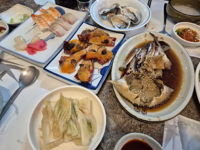 다양한 해산물 요리가 테이블을 가득 채우고 있는 모습. 중앙에는 찜 요리가, 그 주변으로는 샐러드와 젓갈 등이 놓여 있다.