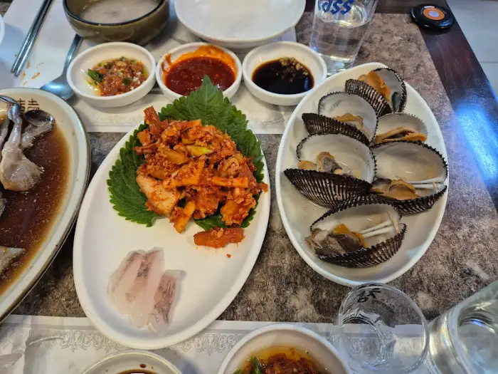 매콤한 양념에 버무려진 해산물 요리와 삶은 조개가 놓인 접시. 곁들임으로 상추와 얇게 썬 생선회가 보인다.