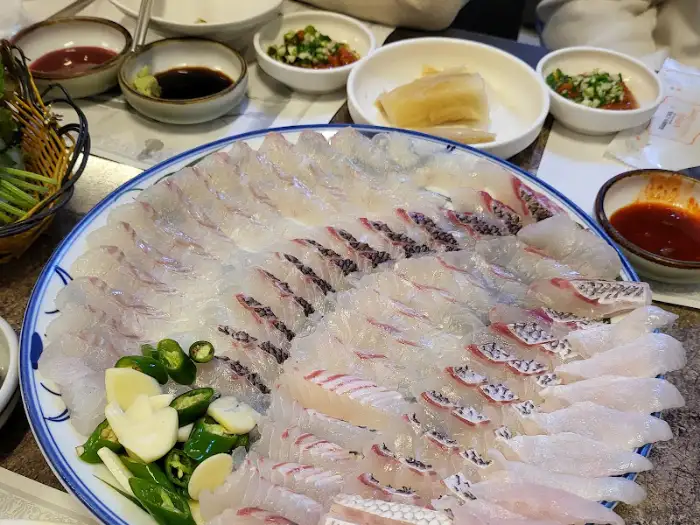 넓은 접시에 겹겹이 쌓인 신선한 회의 클로즈업. 푸른빛이 감도는 생선 살결과 붉은빛이 도는 껍질 부분이 선명하게 보인다.