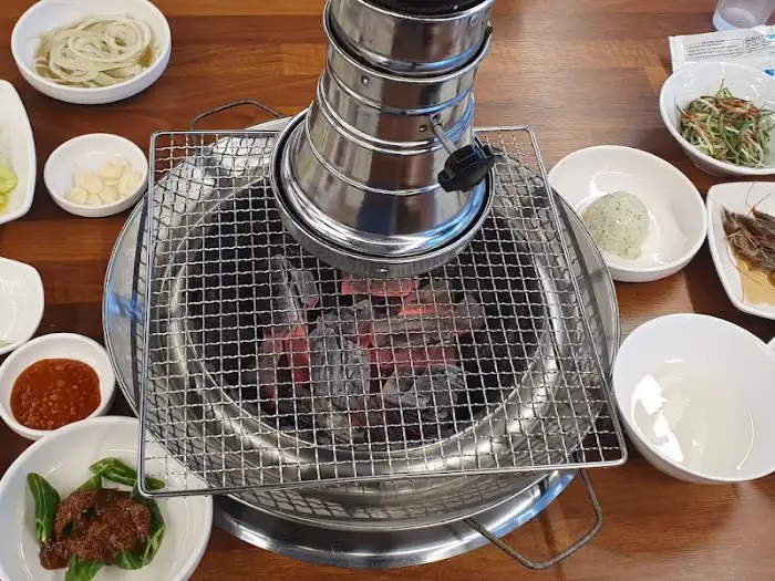 테이블 중앙에 놓인 숯불이 타오르고 있고, 주변에 다양한 그릇과 반찬들이 세팅된 모습