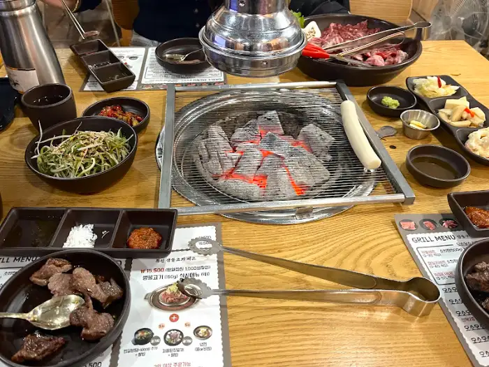 오소오소 서대문 본점의 식사 준비가 된 테이블 모습. 숯불이 피어오르고 다양한 반찬들이 준비되어 있습니다.