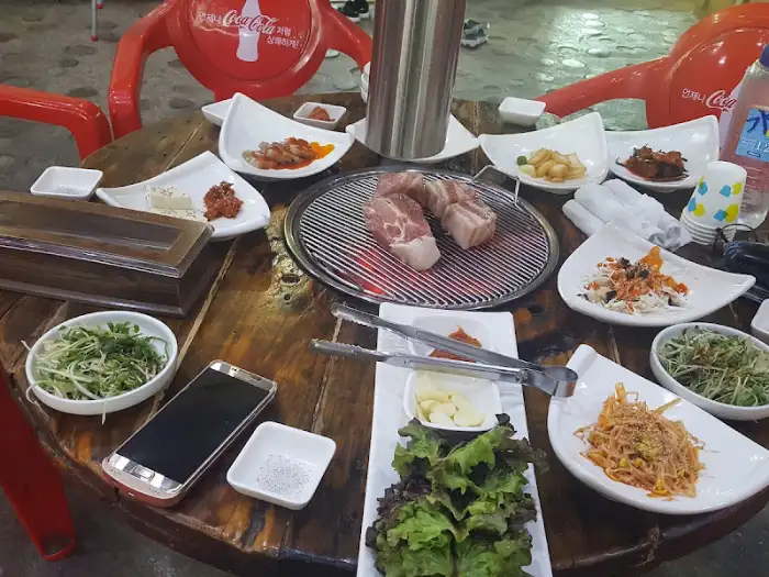 테이블 위에 차려진 삼겹살과 각종 반찬, 그리고 숯불