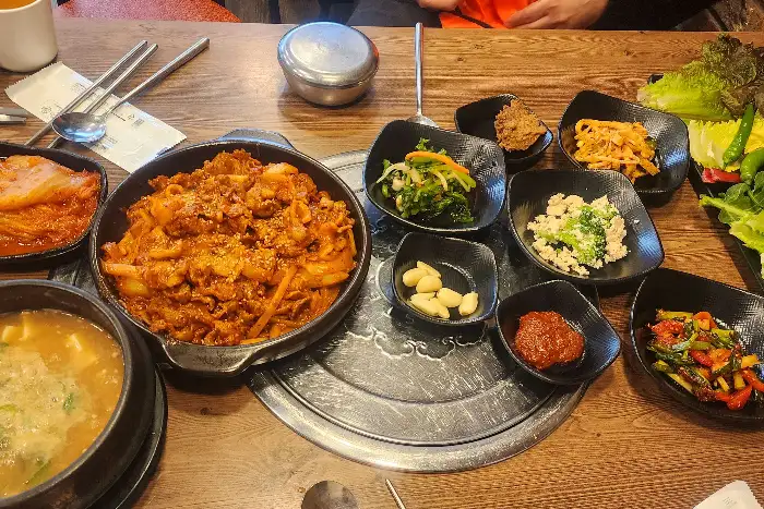 제육볶음, 된장찌개, 생선구이, 다양한 나물 반찬과 쌈 채소가 풍성하게 차려진 한상차림