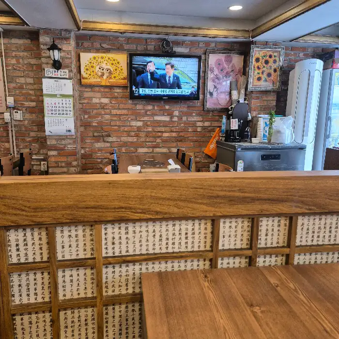 식당 내부 모습, 벽돌 벽과 나무 테이블, 여러 그림들이 걸려 있어 따뜻하고 정겨운 분위기를 연출합니다.