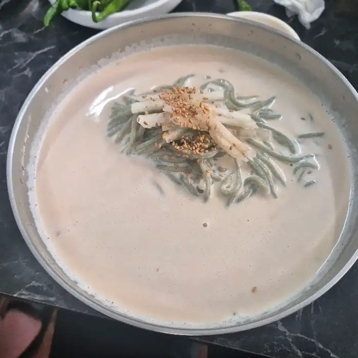 고소한 콩국물 위에 뿌려진 깨소금과 고명이 돋보이는 콩국수