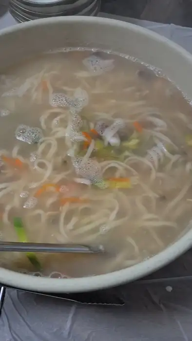 따뜻한 국물의 칼국수가 담긴 큰 그릇과 집게