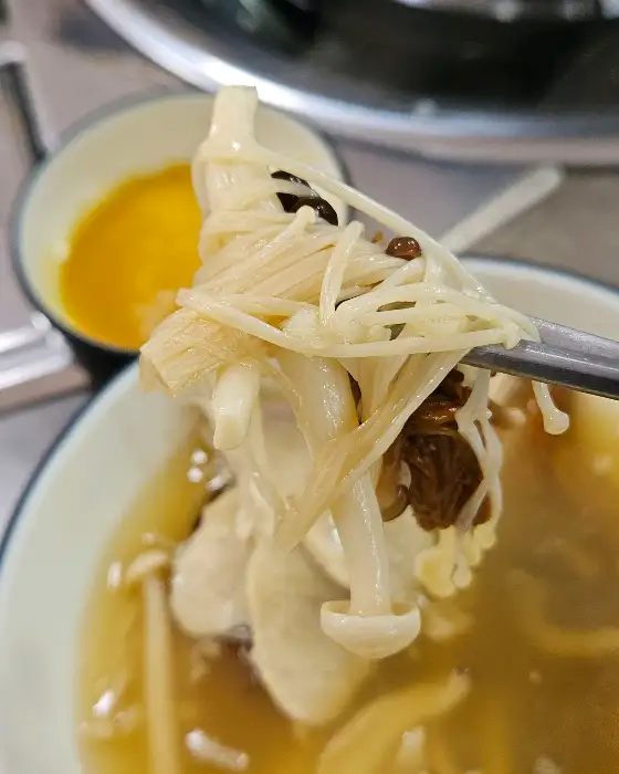 집게에 올려진 버섯과 함께 국물을 떠먹는 모습