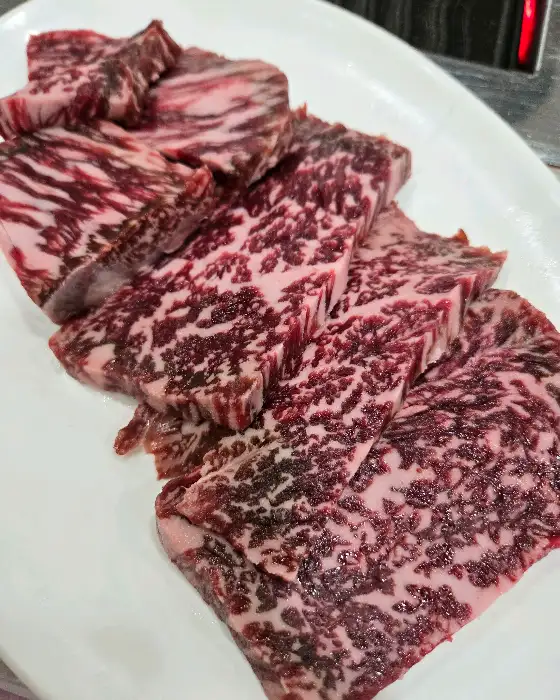 접시 위에 놓인 신선한 약소고기 여러 점을 클로즈업한 모습입니다. 먹음직스러운 마블링이 돋보입니다.