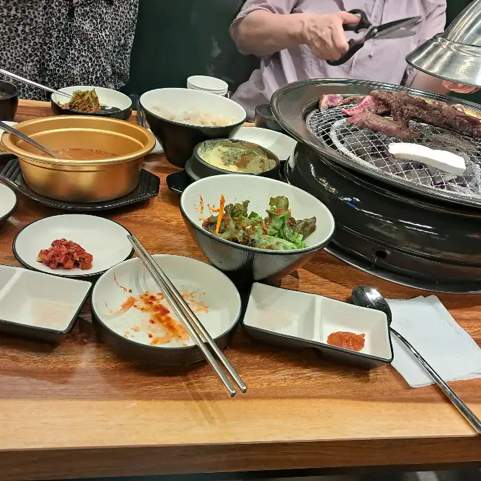 식탁 위에 차려진 다양한 반찬과 덜어 먹는 고기, 그리고 찌개
