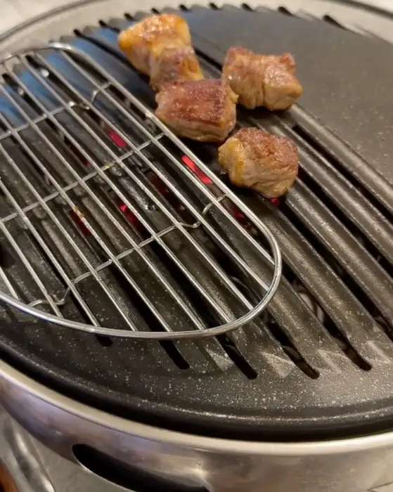 숯불 위에서 맛있게 구워지고 있는 두툼한 고기 덩어리