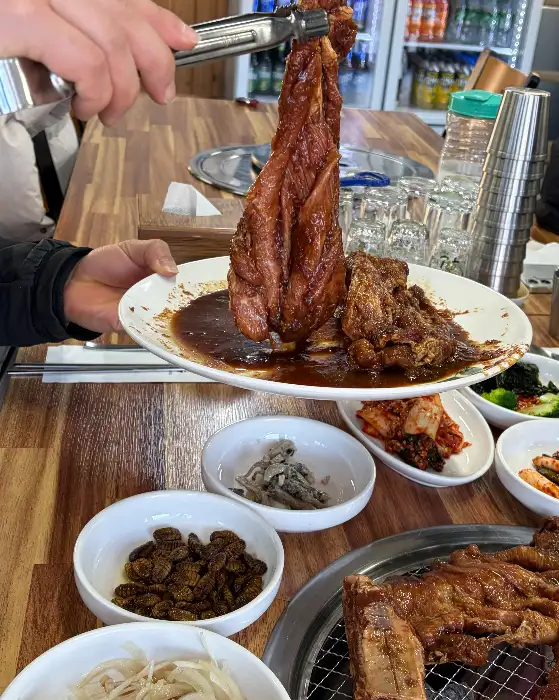 두툼하고 먹음직스러운 양념 돼지갈비를 집게로 들어 올리는 모습
