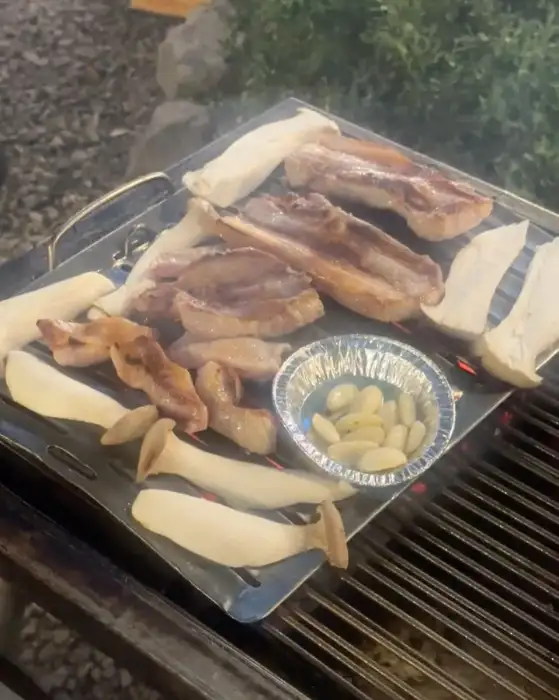 산앤들 야외 테이블에서 굽고 있는 다양한 부위의 고기와 버섯, 마늘