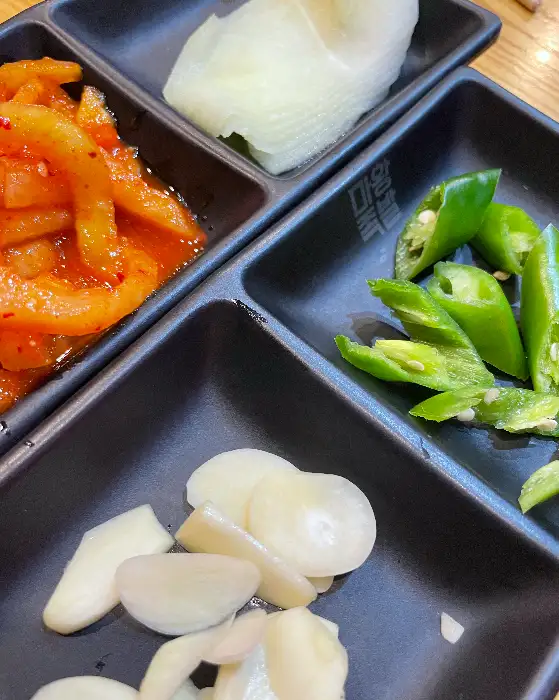 마왕족발 강원고성점의 밑반찬 구성, 쌈무, 마늘, 고추, 김치 등이 준비되어 있습니다.