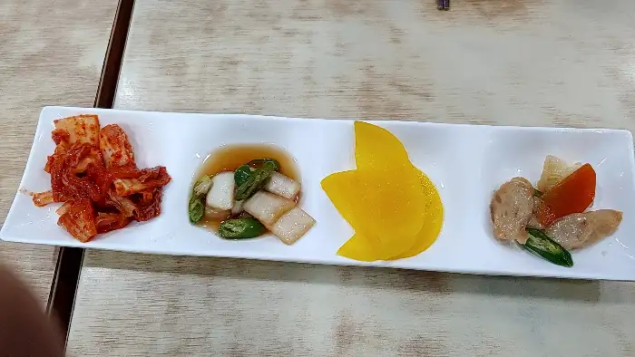 김치, 깍두기, 단무지, 어묵볶음이 정갈하게 담긴 반찬 접시입니다.
