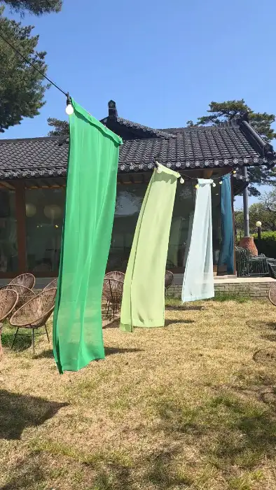 카페 설악산로 야외 공간, 바람에 흔들리는 연두색, 파란색, 초록색 천이 바람에 흩날리고 있습니다.