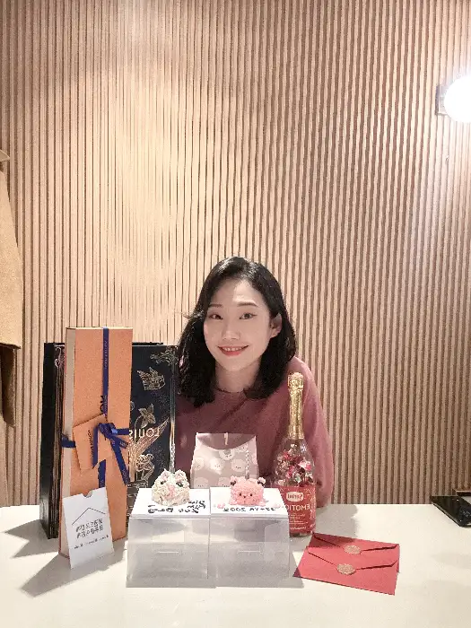 축하 케이크와 선물 상자가 놓인 테이블 앞에 앉은 여성