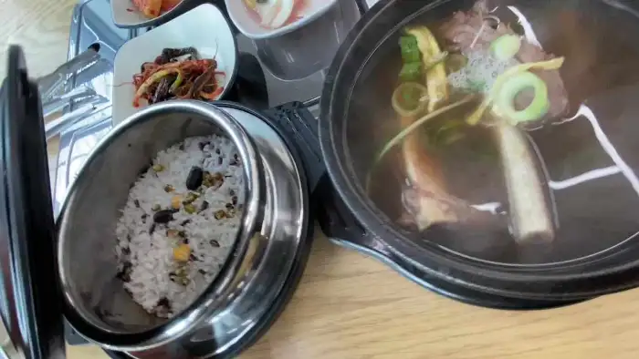 뽀얀 국물의 갈비탕과 밥이 담긴 솥, 그리고 다양한 반찬이 놓인 식탁