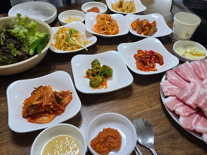 식탁 위에 차려진 다양한 기본 찬과 쌈 채소, 그리고 삼겹살