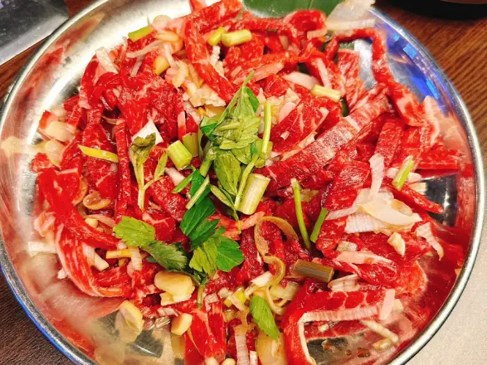 신선한 육회가 푸짐하게 담긴 접시, 고명으로 파와 허브가 올라가 있다