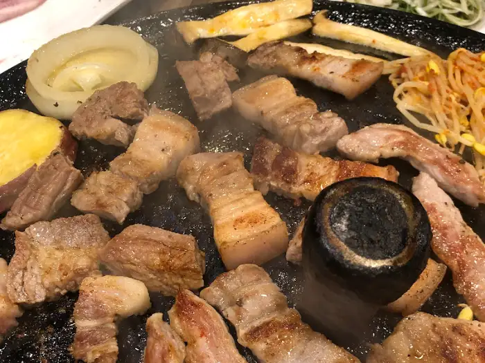 솥뚜껑 위에서 노릇하게 익어가는 삼겹살과 곁들임 재료들