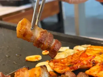 집게로 집어 올린 먹음직스러운 삼겹살 한 점