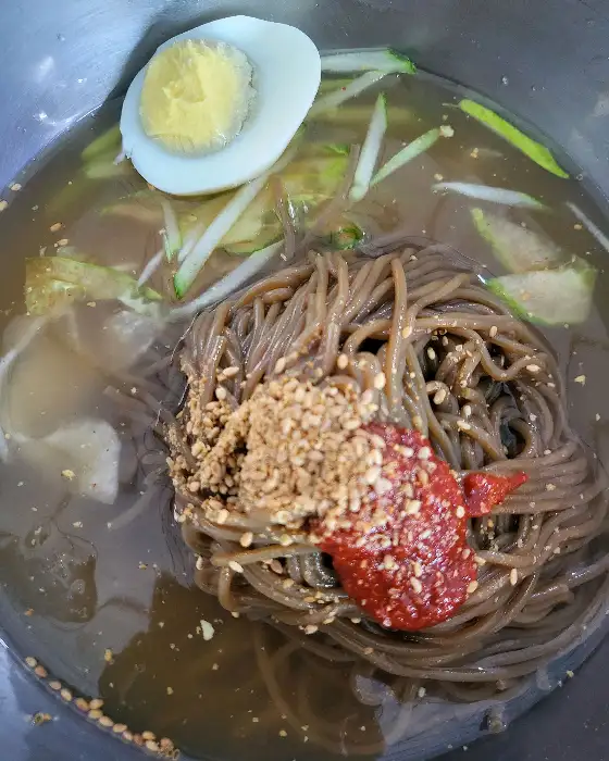 막국수 그릇에 담긴 면과 고명, 국물