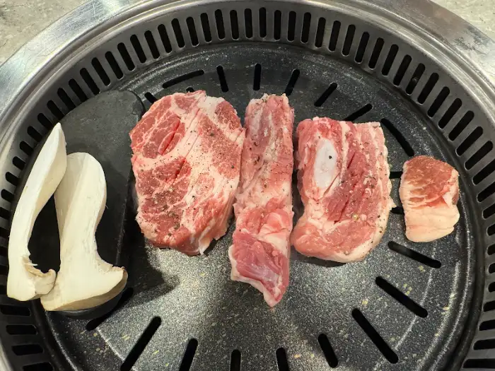 불판 위에 먹음직스럽게 놓인 두툼한 고기 덩어리와 새송이버섯