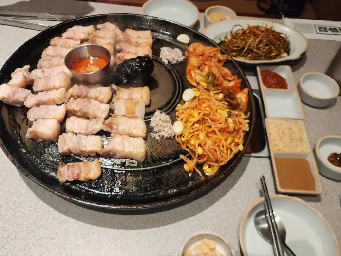 솥뚜껑 위에서 익어가고 있는 삼겹살과 곁들임, 그리고 밥