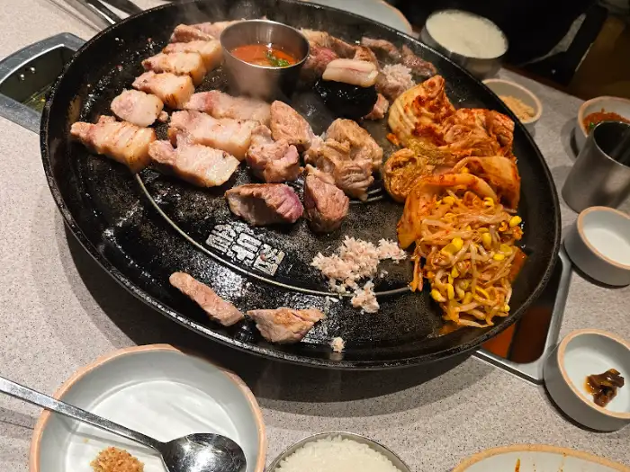솥뚜껑 위에서 거의 다 익은 삼겹살과 곁들임