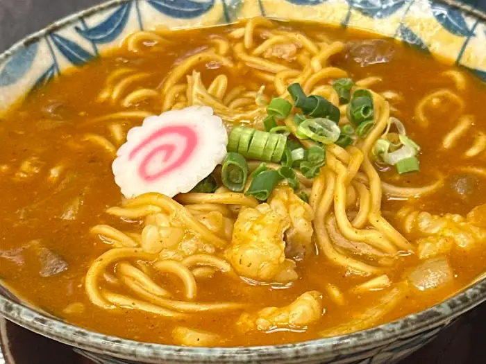 카레 우동에 덴푸라 새우와 나루토마키가 올려진 모습