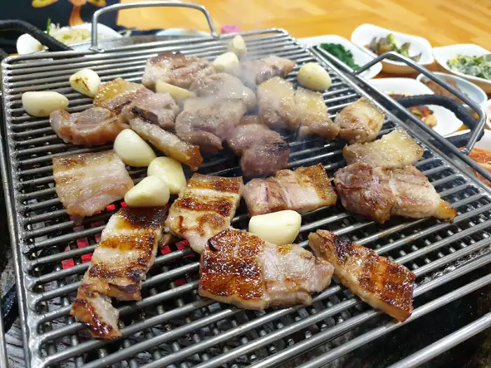 숯불에 구워지는 삼겹살과 마늘, 그리고 다양한 밑반찬