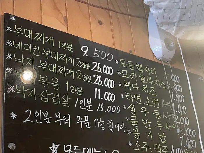 매장 벽면에 걸린 검은색 메뉴판에 다양한 부대찌개와 곁들임 메뉴가 적혀 있습니다.